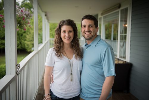 man-and-woman-stand-on-porch-embracing