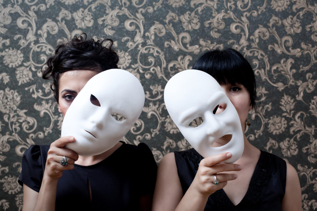 Two women peeking behind mask on wallpaper background