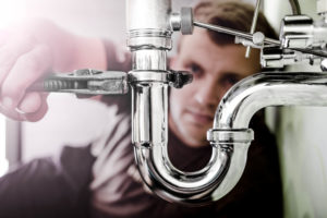 Plumber using a wrench to tighten a siphon under a sink.