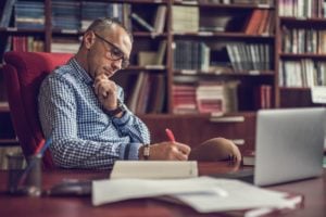 man-works-in-academic-office-with-bookshelves-and-desk