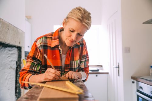 A woman wearing an orange flannel shirt works on a kitchen renovation project.