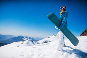 young woman stands on top of mountain holding a snowboard