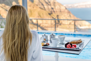 Horizontal color image of charming woman sitting at terrace and watching the beauty of nature in Santorini. Fresh breakfast in the morning.