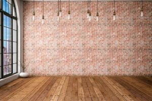 Room with wooden floor and brick wall, and bare bulbs hanging from the ceiling.