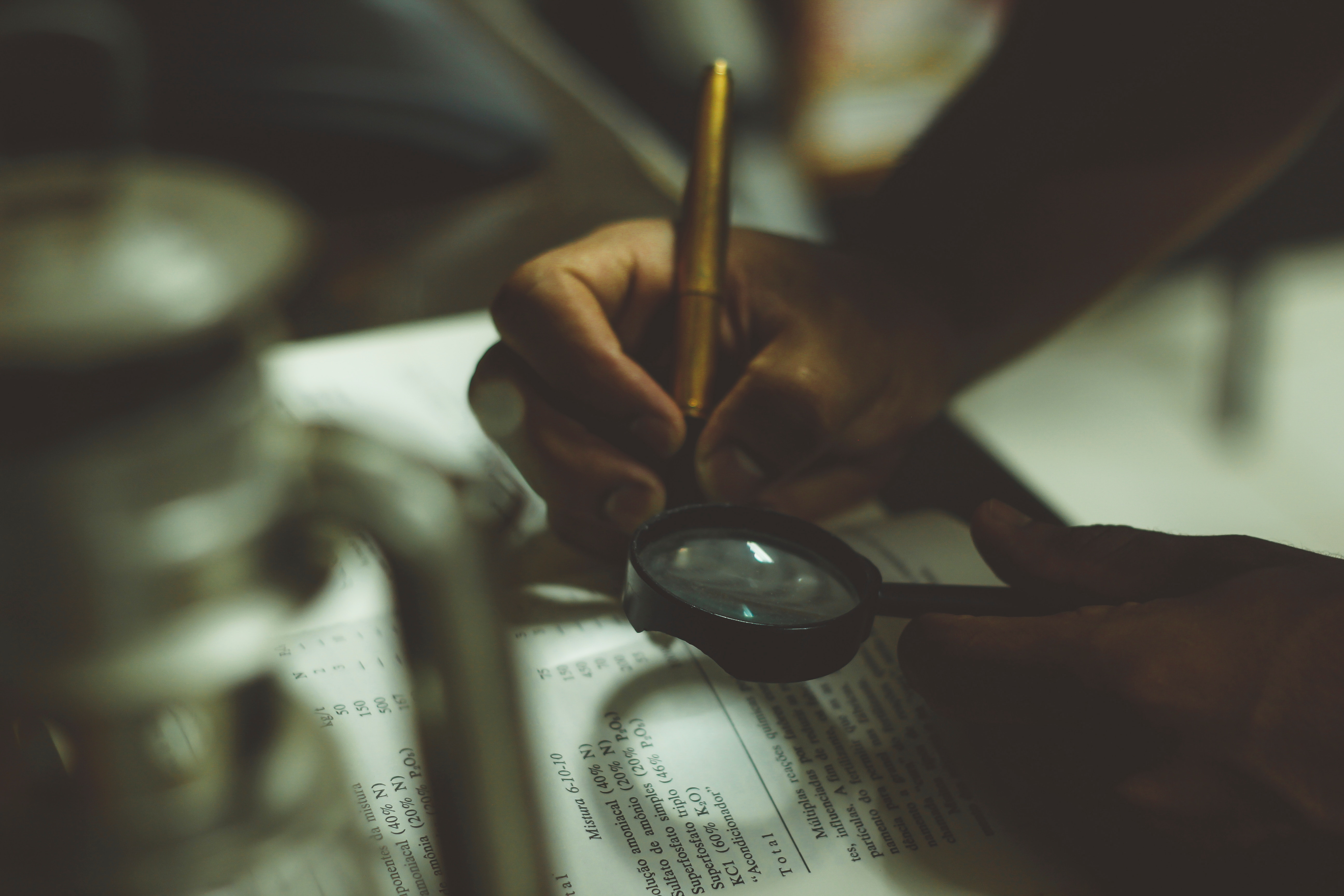 person-annotating-book-with-pen-and-magnifying-glass