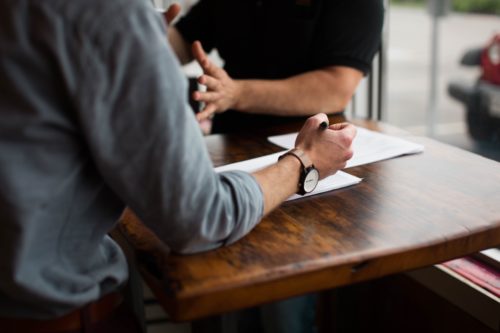 Selective focus photography of two people at a wooden table with paper documents.